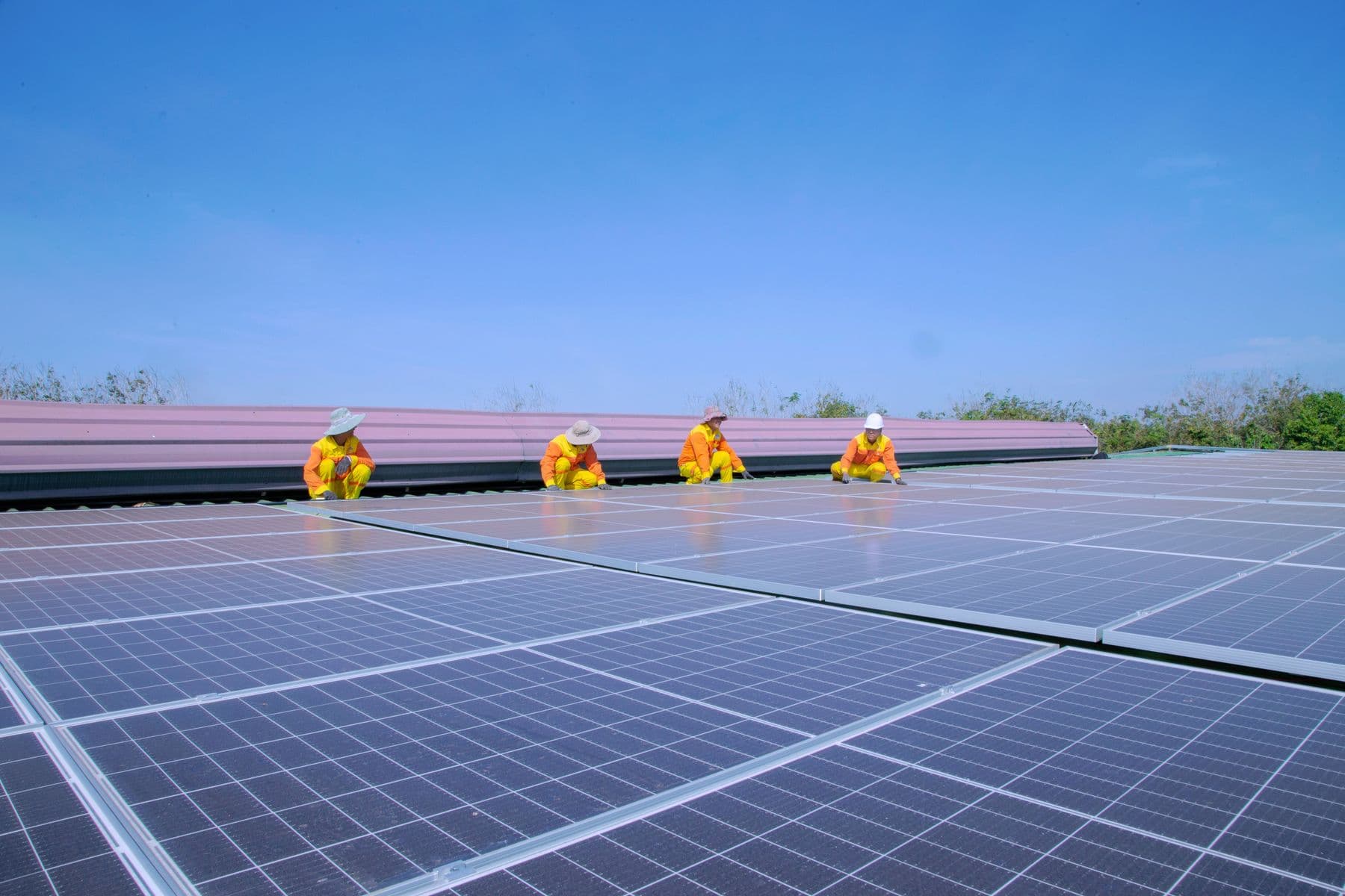 Equipe instalando painéis fotovoltaicos em telhado sob céu azul