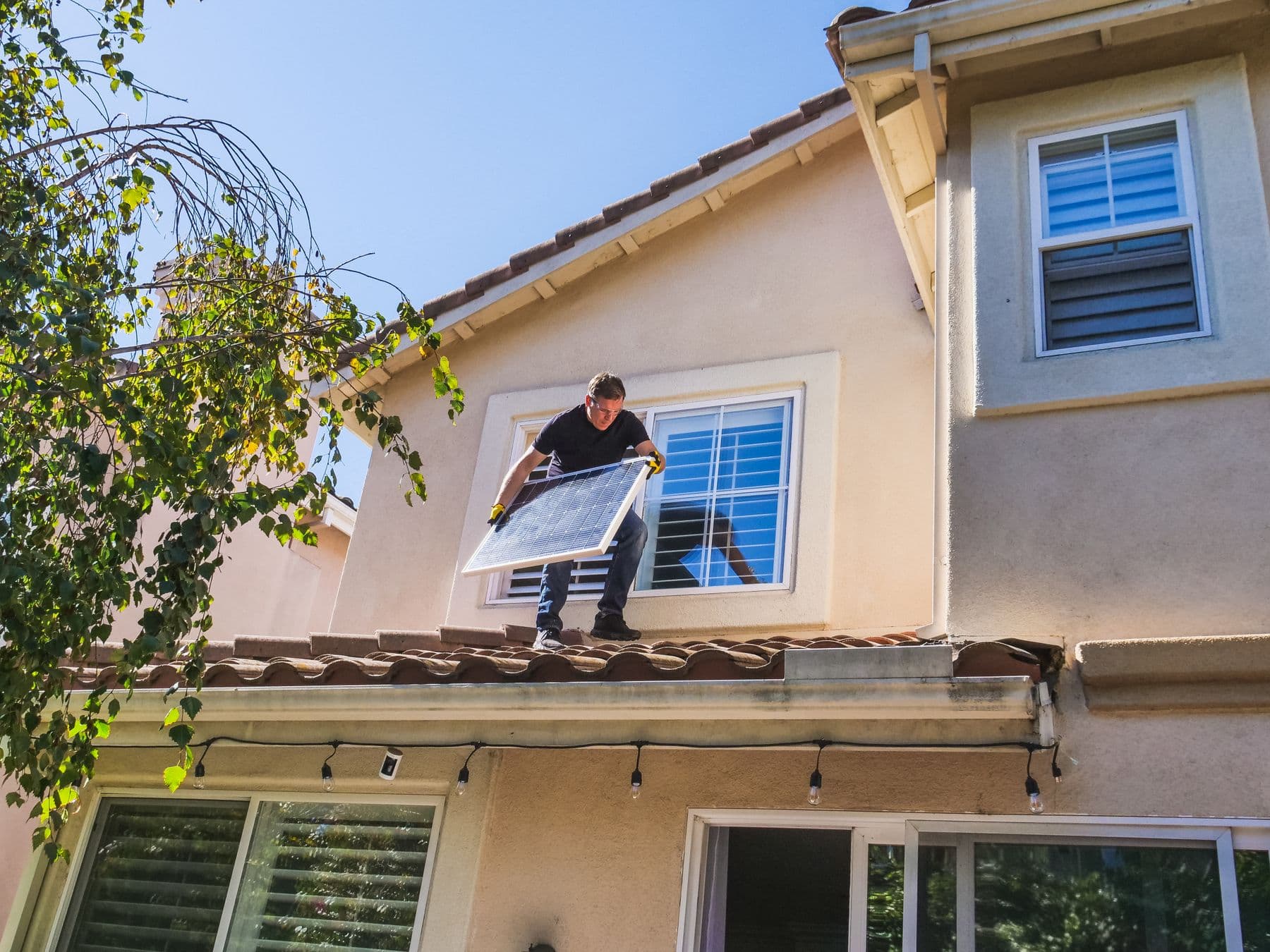 Instalador no telhado de uma casa carregando um módulo fotovoltaico